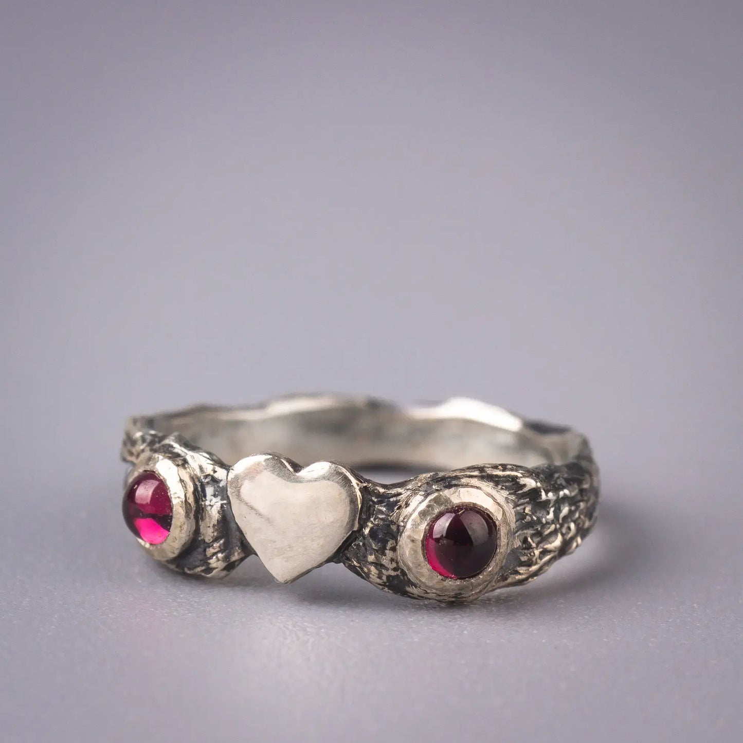 heart twig ring with 2 garnet gemstones on the sides, on a grey background.