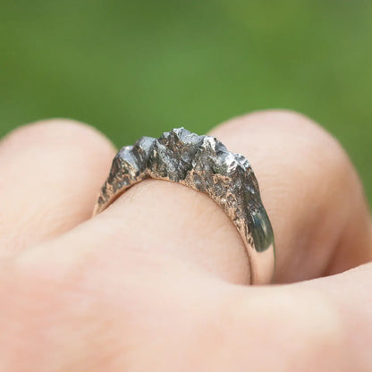 Sterling silver mountain range ring with organic rock texture worn on finger against a green background.