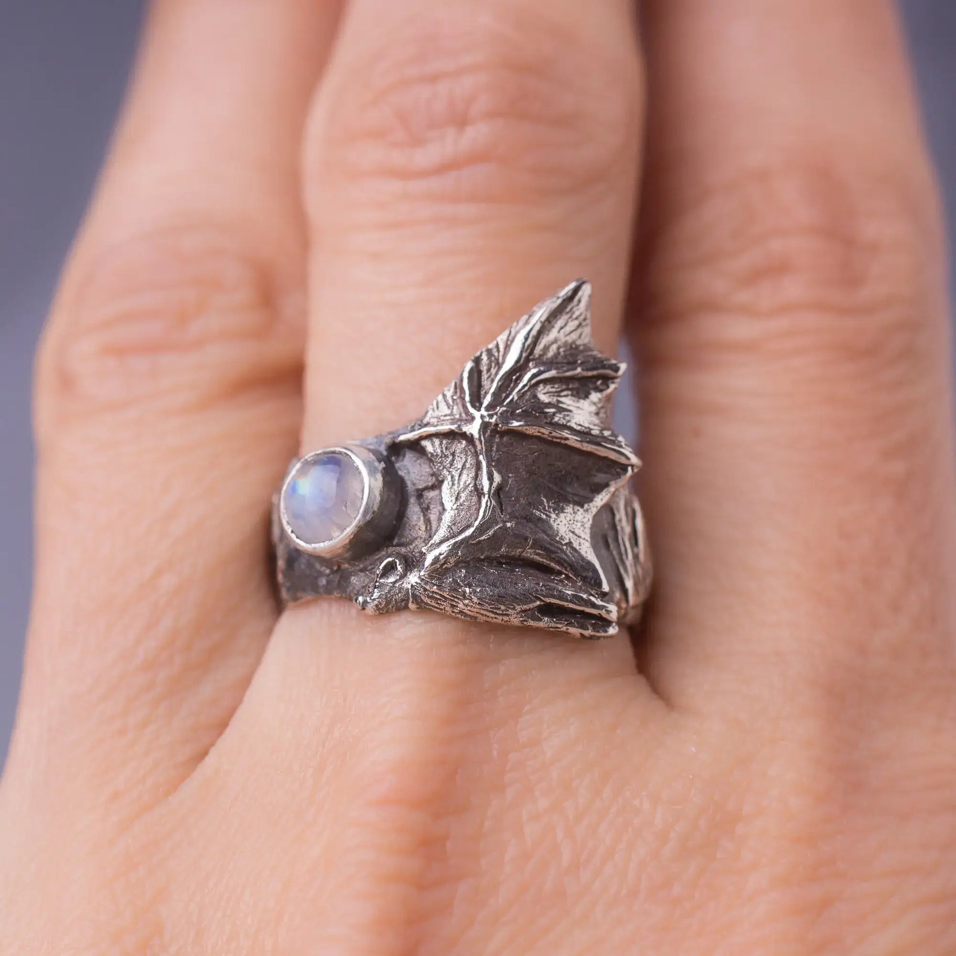 Sterling silver bat ring with intricate wings and a gemstone on a person's finger