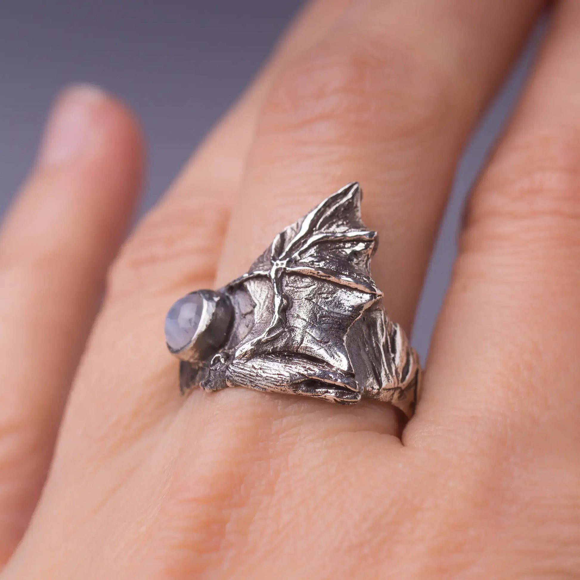 Sterling silver bat ring with gemstone showcasing detailed bat wings wrapped around a finger.