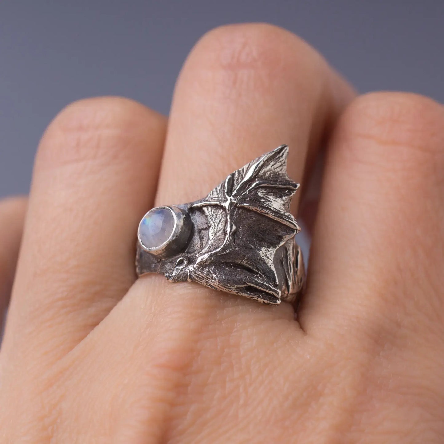 Sterling silver bat ring with a gemstone featuring detailed bat wings, worn on a finger.