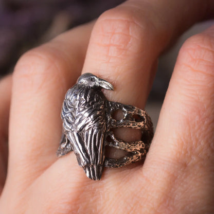 Silver crow ring with intricate design on hand, featuring a crow perched on branches, handcrafted using lost wax technique.