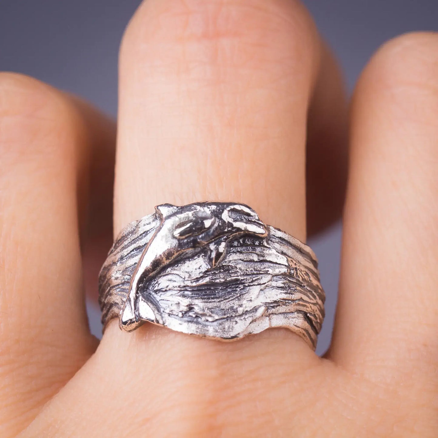 Sterling silver dolphin ring with a wide, wavy band on a finger, capturing ocean-inspired sea life with a lifelike bottlenose dolphin design.