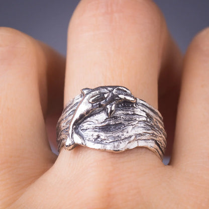 Sterling silver dolphin ring with wavy wide band on hand, ocean-inspired design, lifelike bottlenose dolphin detail.