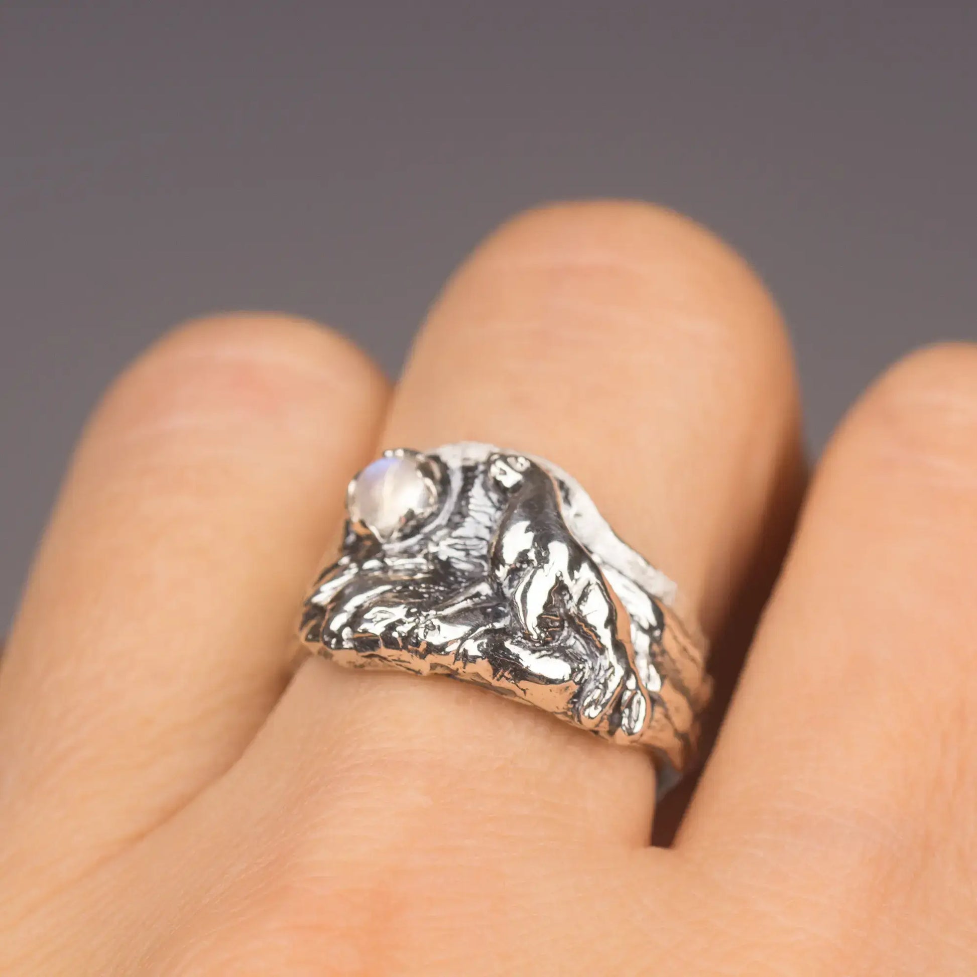 Sterling silver sea lion ring set with moonstone on finger, featuring intricate ocean and rocky beach design.