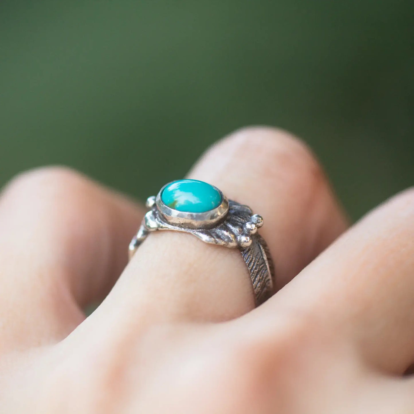 Thunderbird ring with turquoise oval gemstone and sterling silver feather design, worn on a finger.