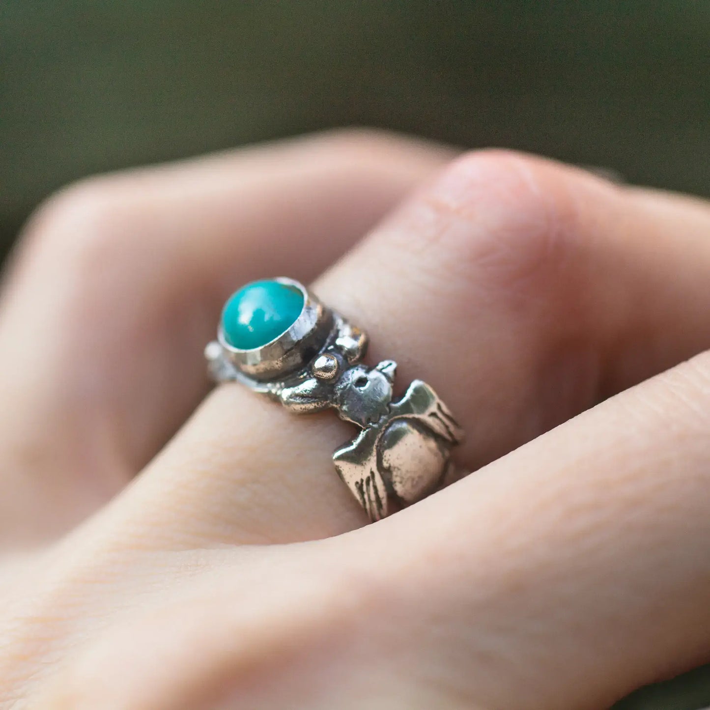 Thunderbird turquoise oval gemstone sterling silver ring with feather design worn on finger.