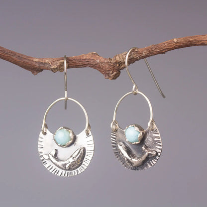 Silver humpback whale dangle earrings with larimar gemstone, handmade ocean style jewelry displayed on a rustic branch.