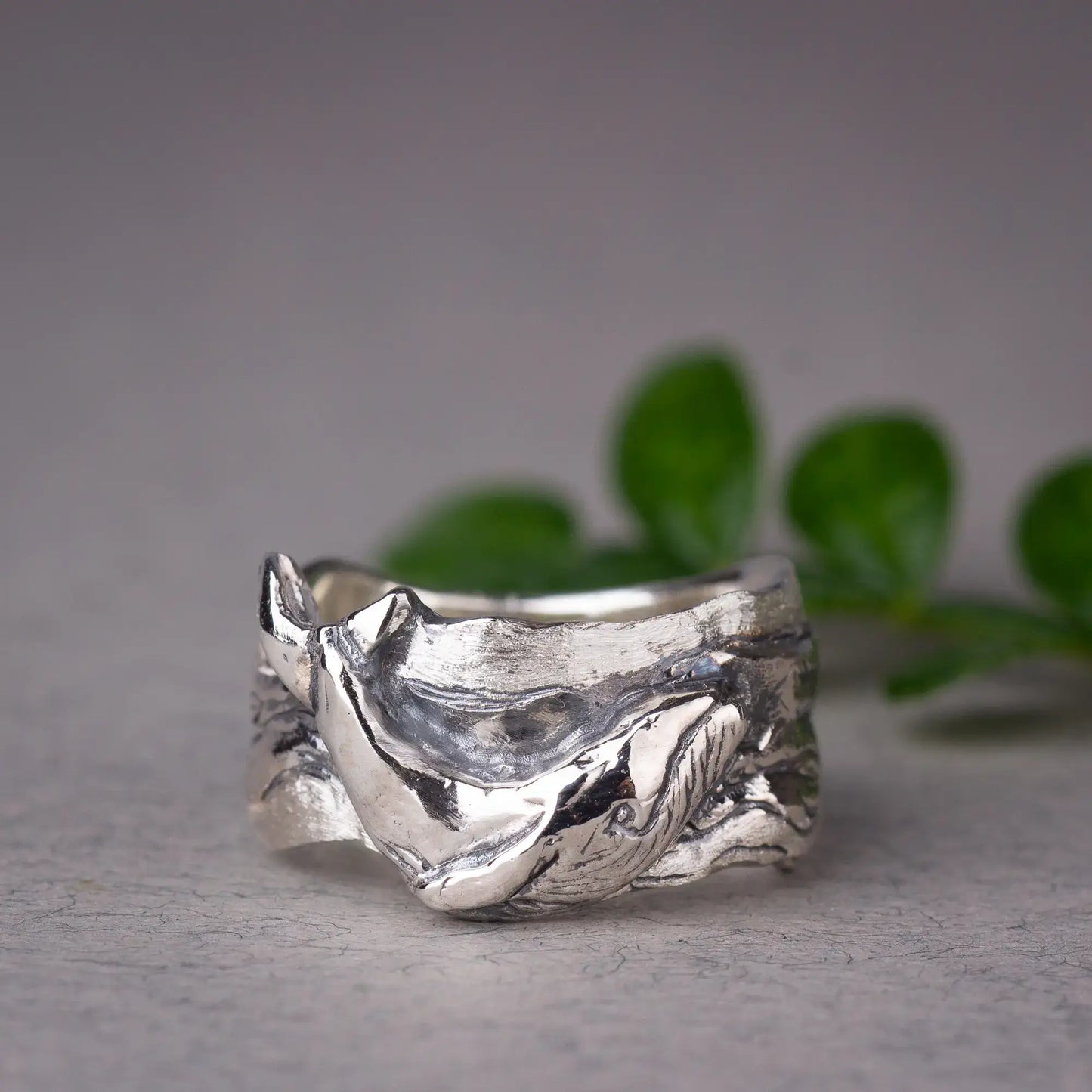 Sterling silver whale ring featuring a detailed humpback whale design, wide band ocean ring on display with green leaves in background