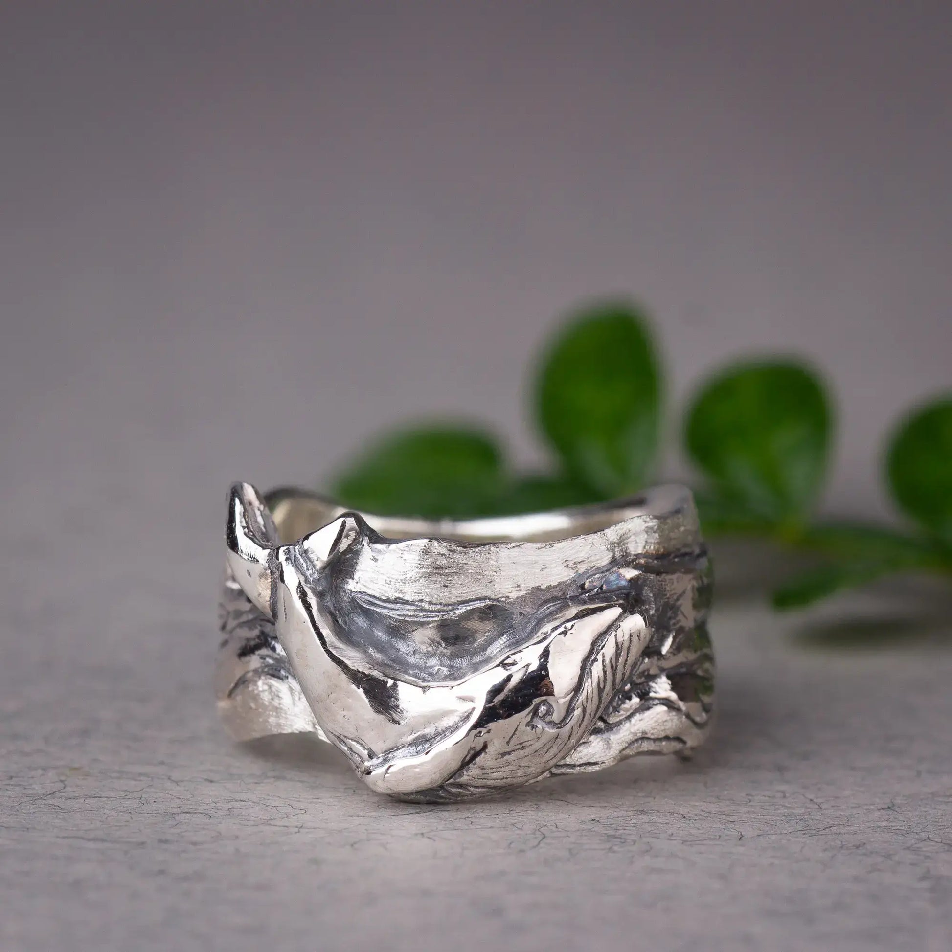 Sterling silver whale ring featuring a detailed humpback whale design, wide band ocean ring on display with green leaves in background